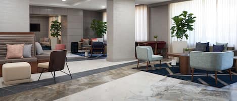 A spacious lobby with a modern design, featuring a large seating area with sofas and chairs, a coffee table, and potted plants.
