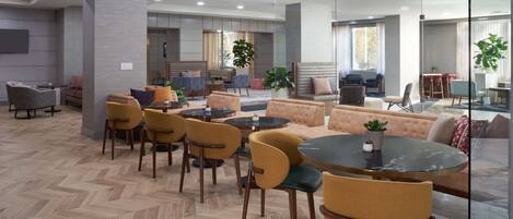 Un área de estar moderna con diversas opciones de asientos, incluyendo sofás y sillones, una mesa redonda y un suelo con estampado tipo espiga.