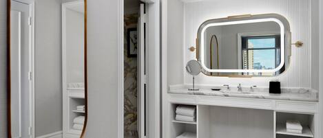 A modern bathroom with a large mirror, a vanity with a sink, and built-in shelves for towels.