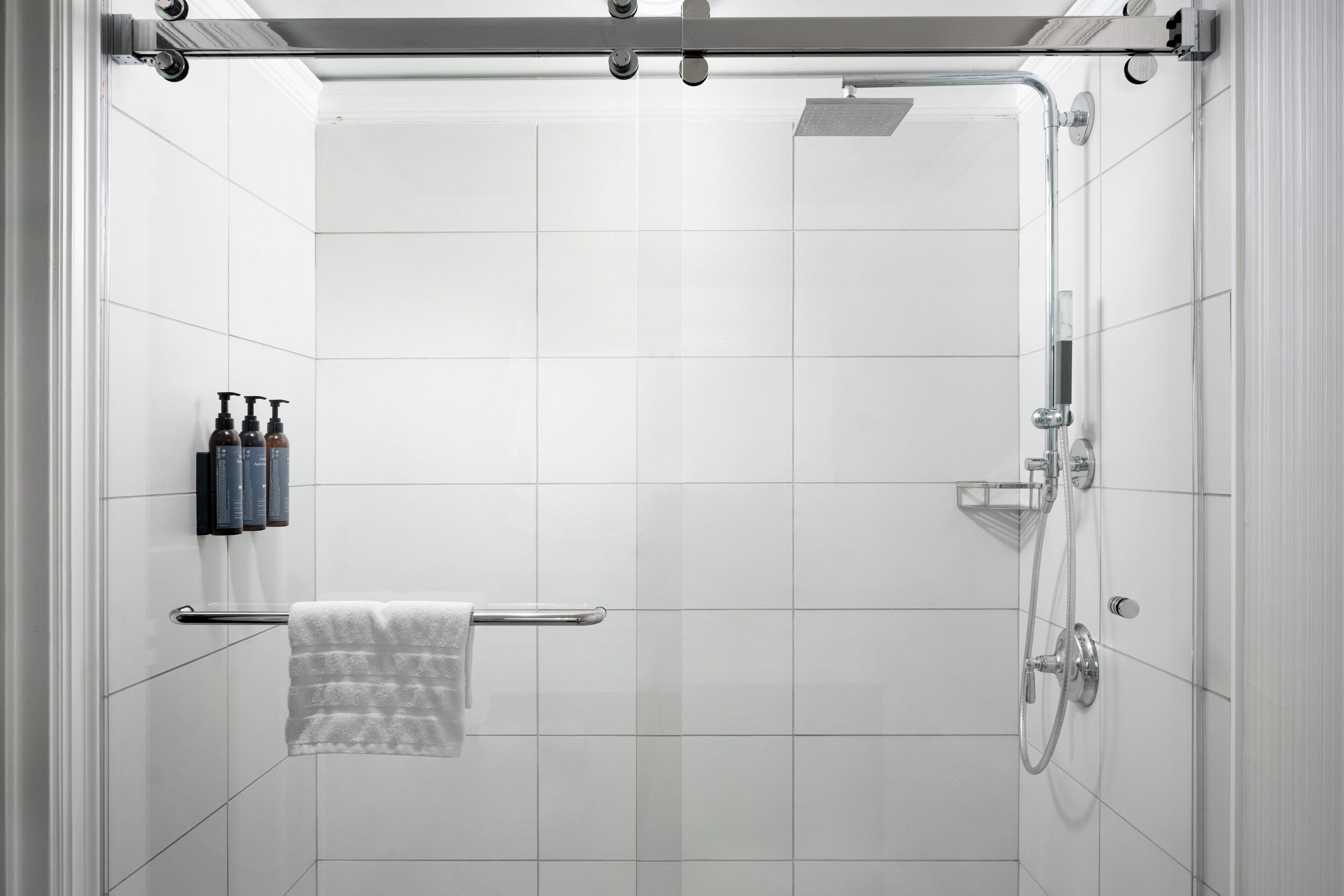 A modern shower with a glass door, a towel rack with a towel, and a set of toiletries on the wall.
