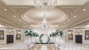 Ein prunkvoller Saal mit einer zentralen Gang, weißen Stühlen, einer Kristallleuchter und floralen Dekorationen.