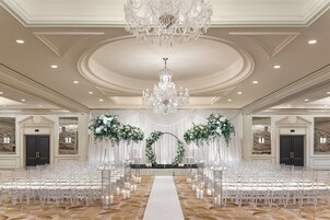 A grand hall with a central aisle, white chairs, a chandelier, and floral decorations.