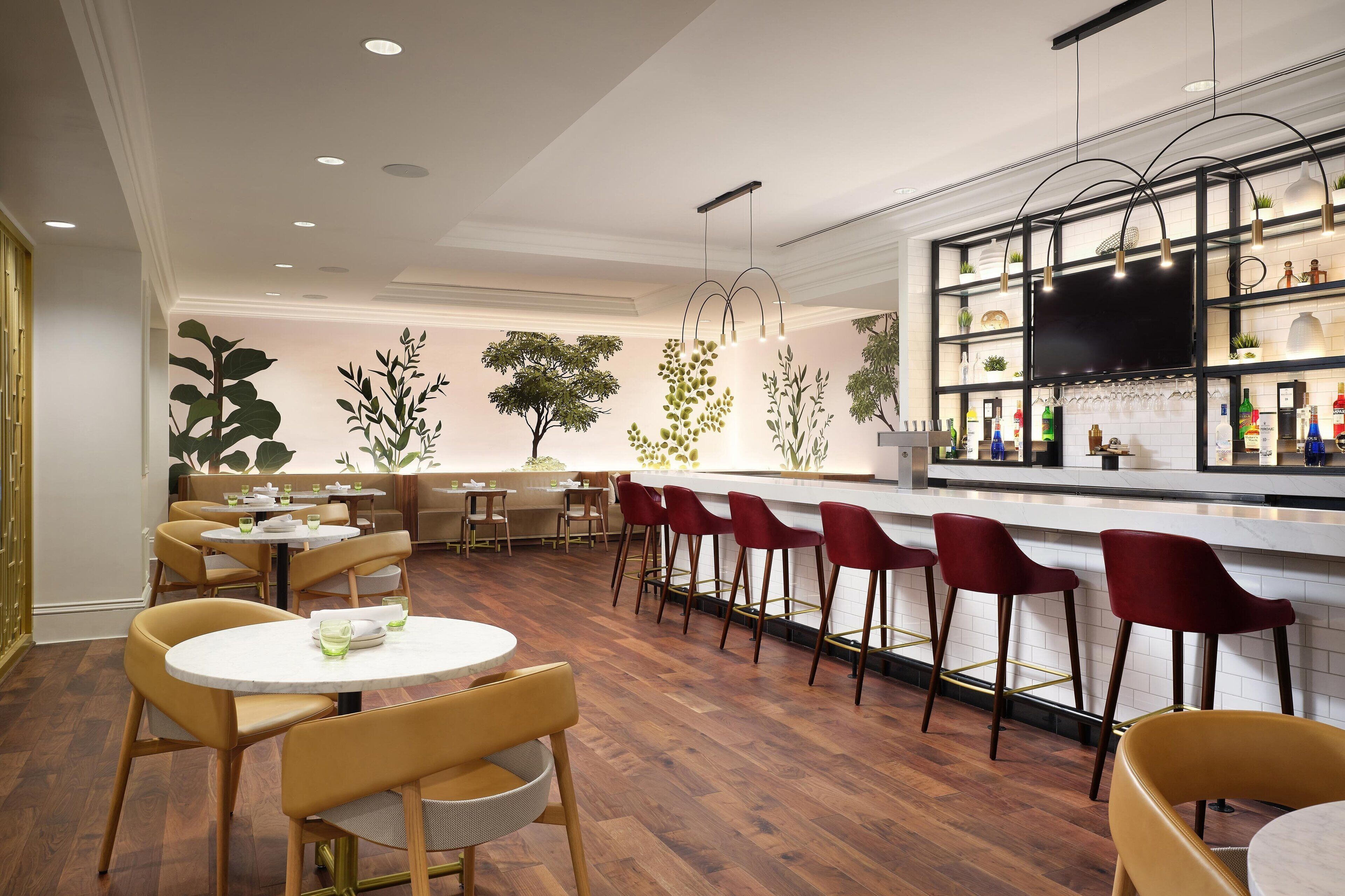 Uma área de bar moderna com piso de madeira, mesas redondas e banquetas vermelhas.