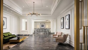 Eine großzügige Lobby mit Marmorboden, einem grünen Sofa, einem beigen Sessel und einer Kronleuchter.