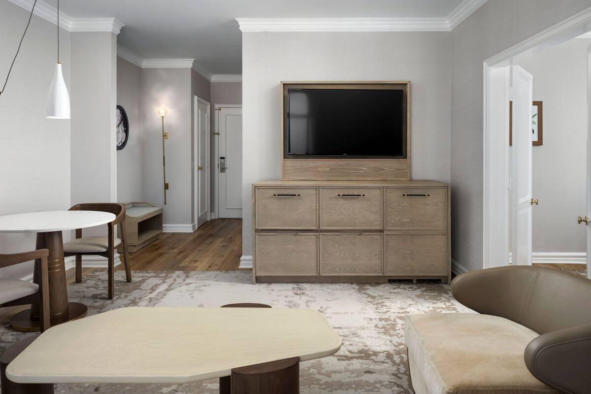 A modern living room with a flat-screen TV, wooden cabinet, and a round table with chairs.