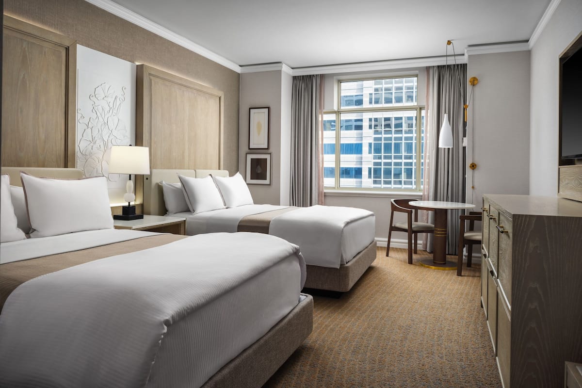A hotel room with two beds, a desk, a chair, a TV, and a window with curtains.