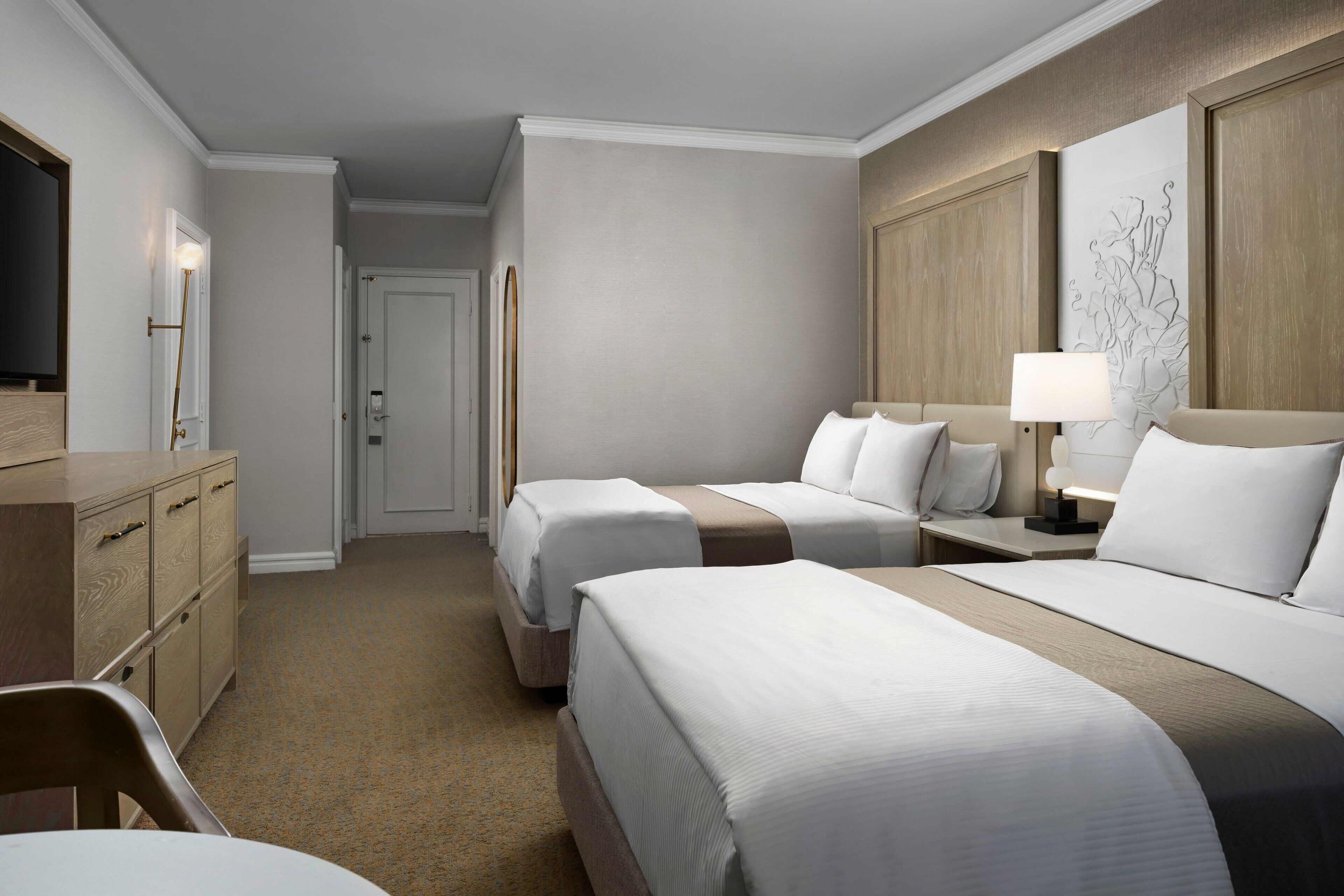 A hotel room with two beds, a desk, a dresser, and a television.