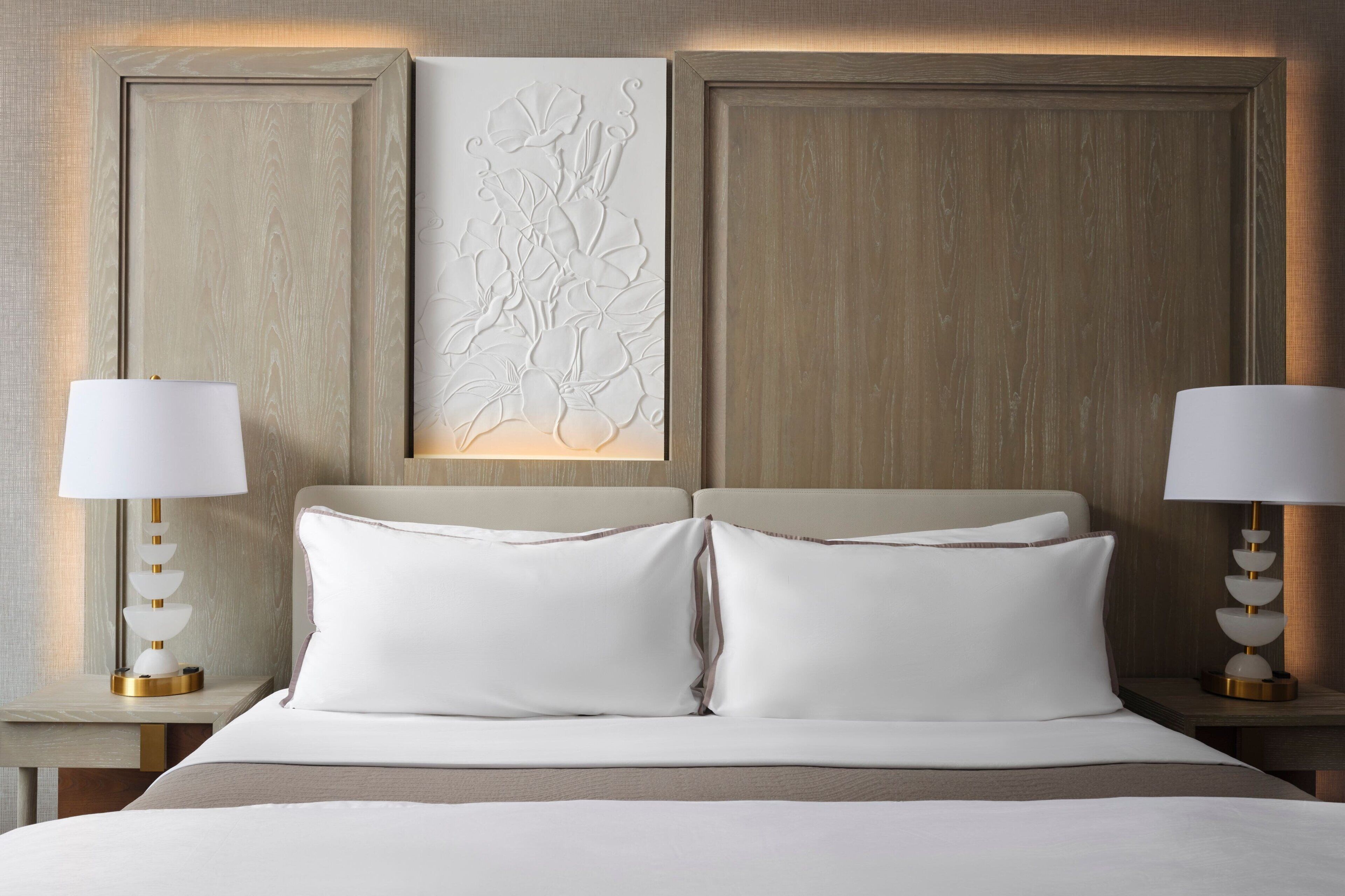 A neatly made bed with white linens and two bedside lamps.