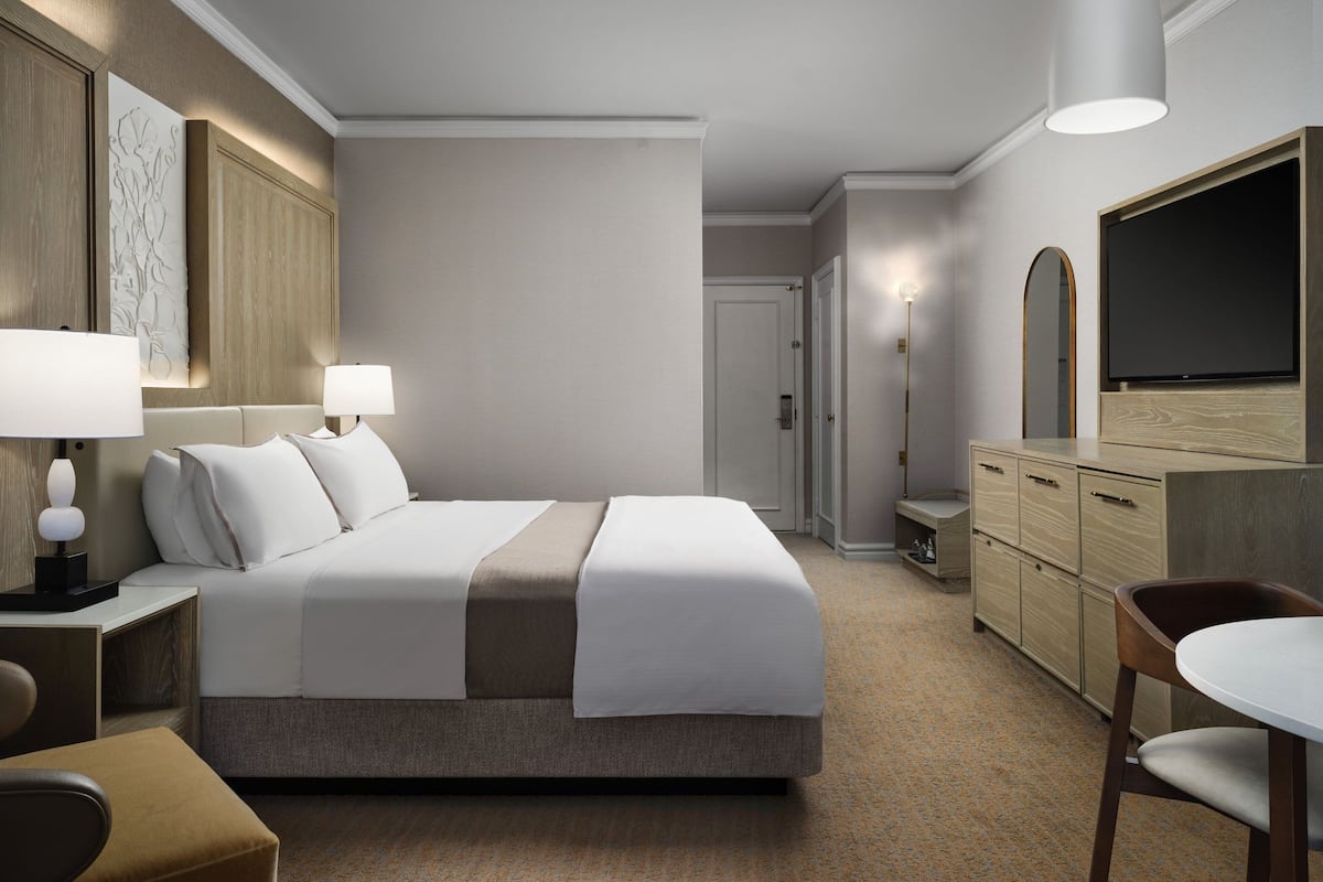 A hotel room with a bed, bedside lamps, a TV, a desk, and a chair.