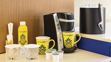 Uma bancada de cozinha com uma cafeteira, uma caneca, uma garrafa e uma caneca com tema de abacaxi.