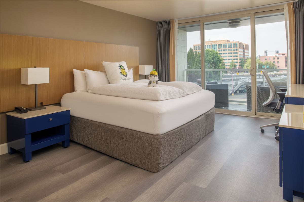 A hotel room with a large bed, a desk, and a view of the city through a large window.
