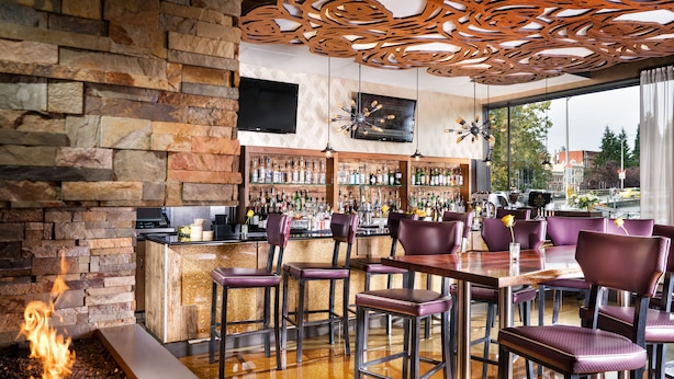 A bar area with a stone wall, a fire feature, and a bar stocked with bottles. - Staypineapple, Hotel Rose, Downtown Portland (Portland)