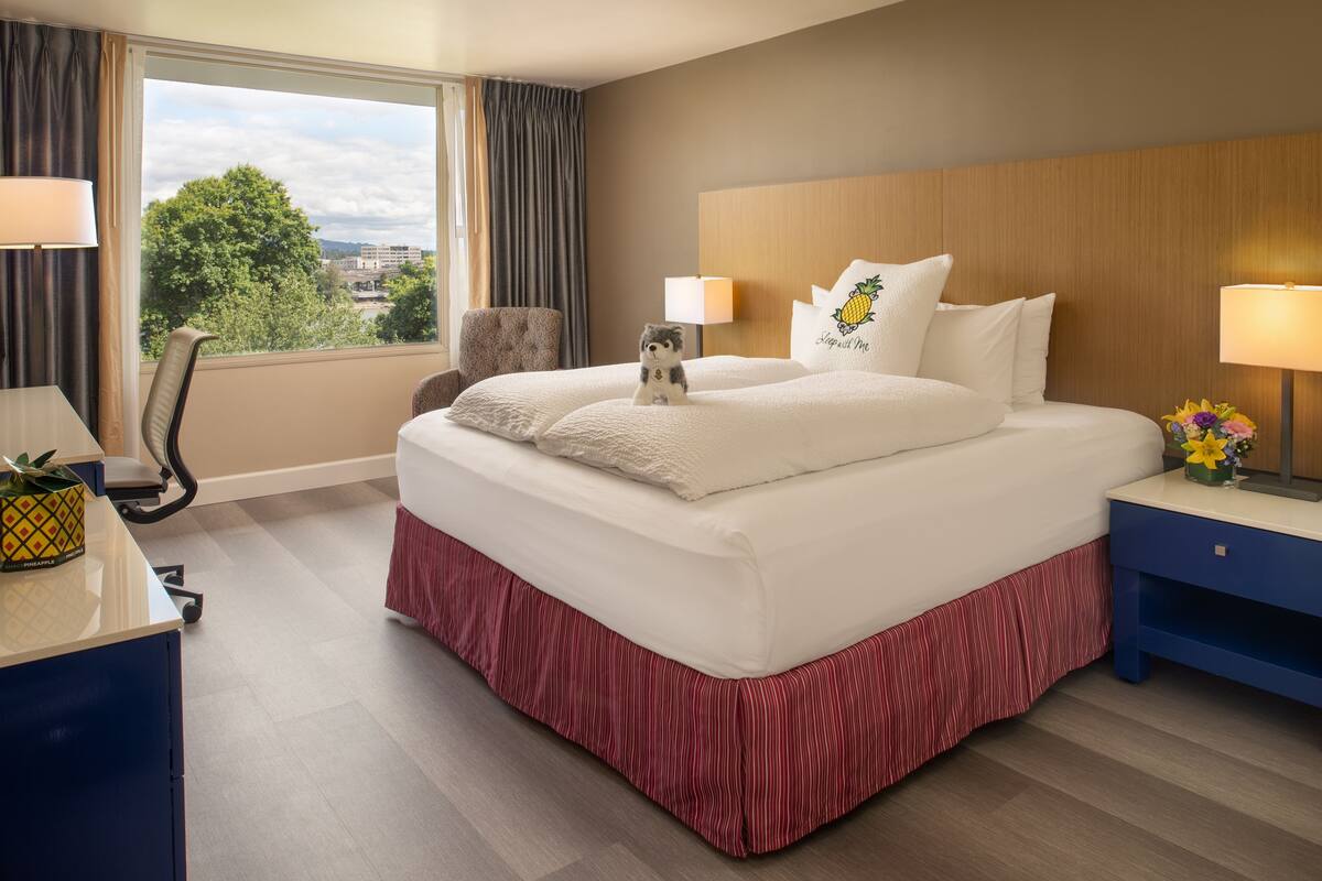 A hotel room with a large bed, a desk, a chair, and a view of the city through the window.