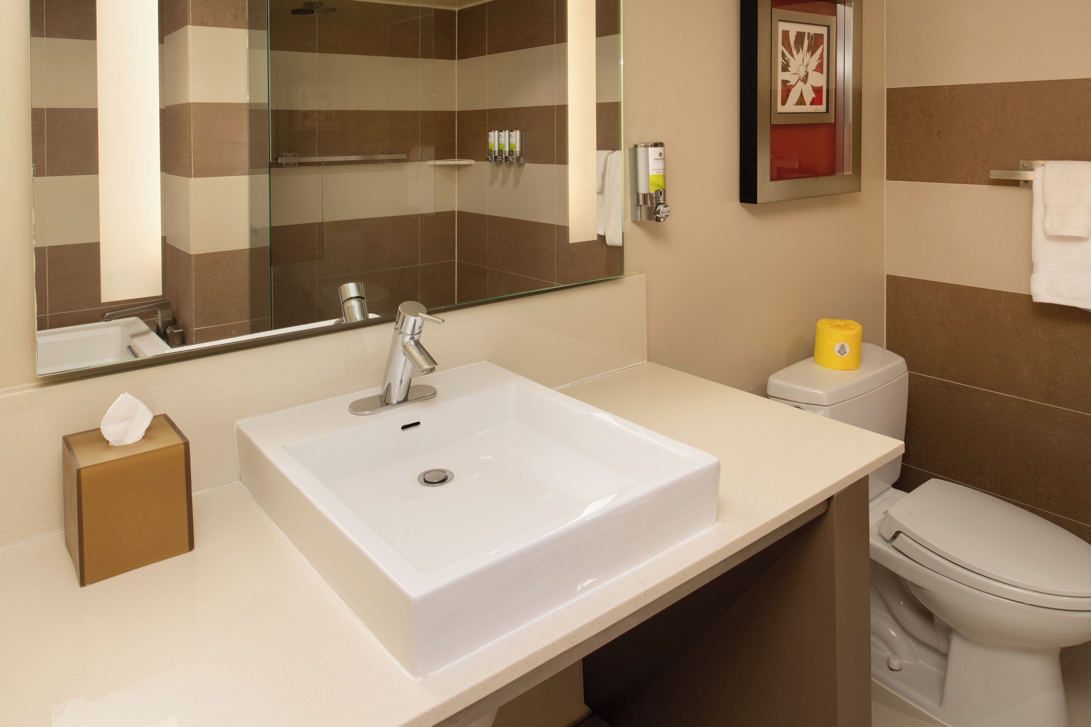 A modern bathroom with a large mirror, a white sink, a toilet, and a shower area.
