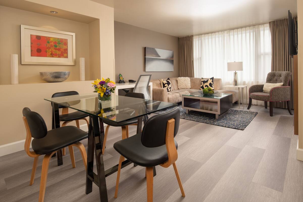 A modern living room with a glass dining table, black chairs, a sofa, and a TV.
