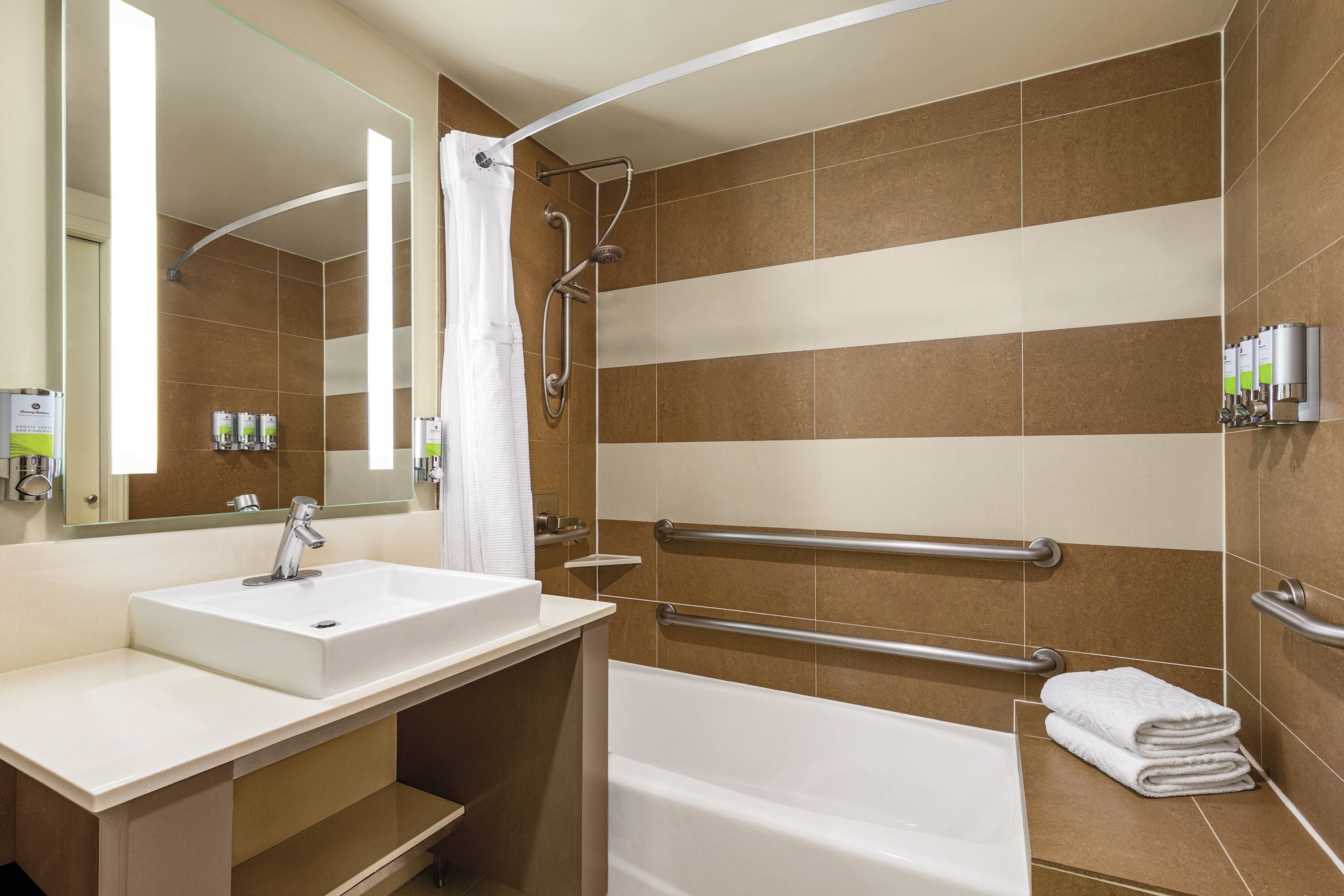 A bathroom with a sink, mirror, shower, and grab bars.