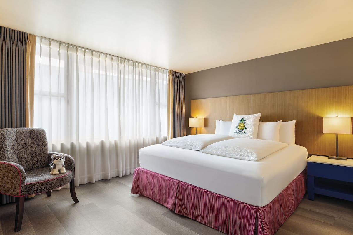 A hotel room with a large bed, a chair, a nightstand, and a lamp.