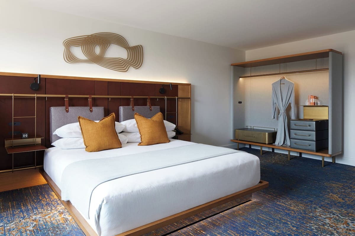 A modern hotel room with a large bed, wooden headboard, and a built-in wardrobe with a mirror and drawers.
