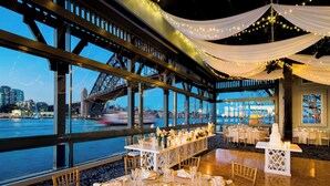 Un comedor con mesas dispuestas para un evento formal, con vistas a un río y un puente al fondo.