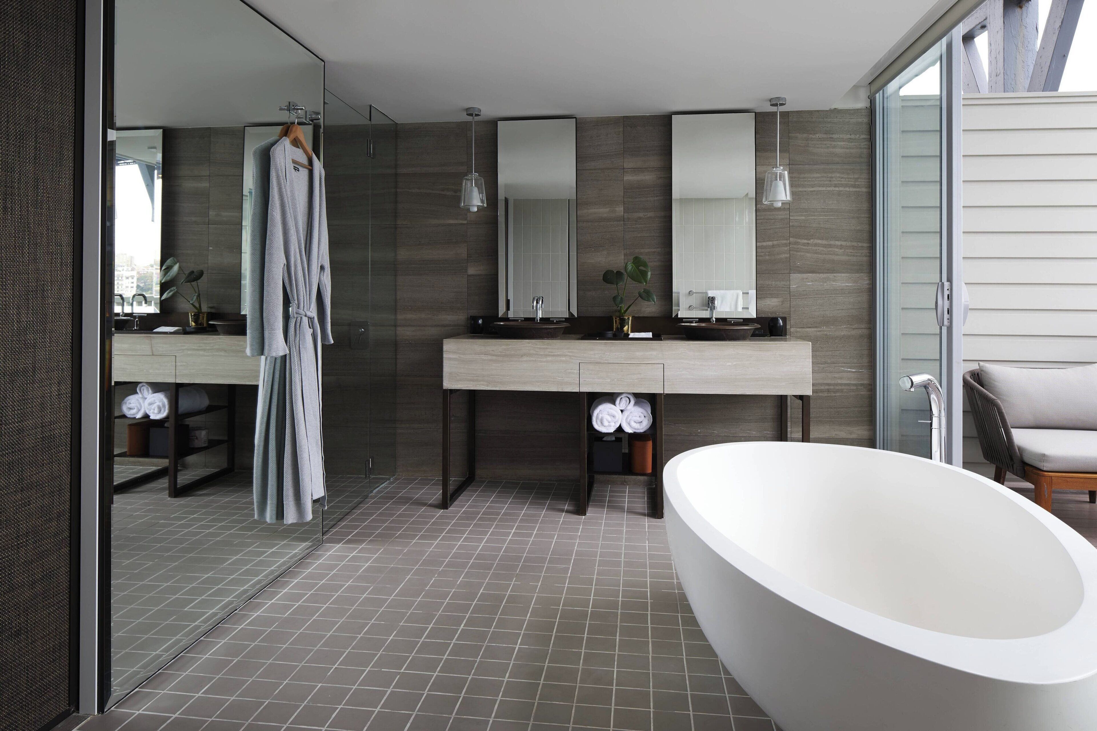 Ein modernes Badezimmer mit einer freistehenden Badewanne, einem großen Spiegel und einem Bademantel auf einem Wäscheständer.