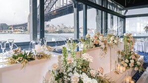 Mesa dispuesta para una recepción de boda, con vista a un puente y al paisaje urbano.