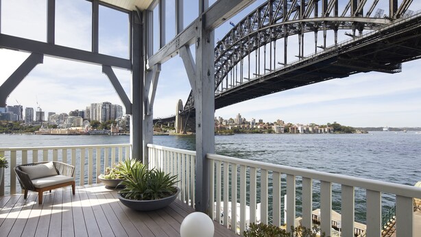 Una terraza con sofá y plantas en macetas, con vistas a un horizonte urbano y un puente.