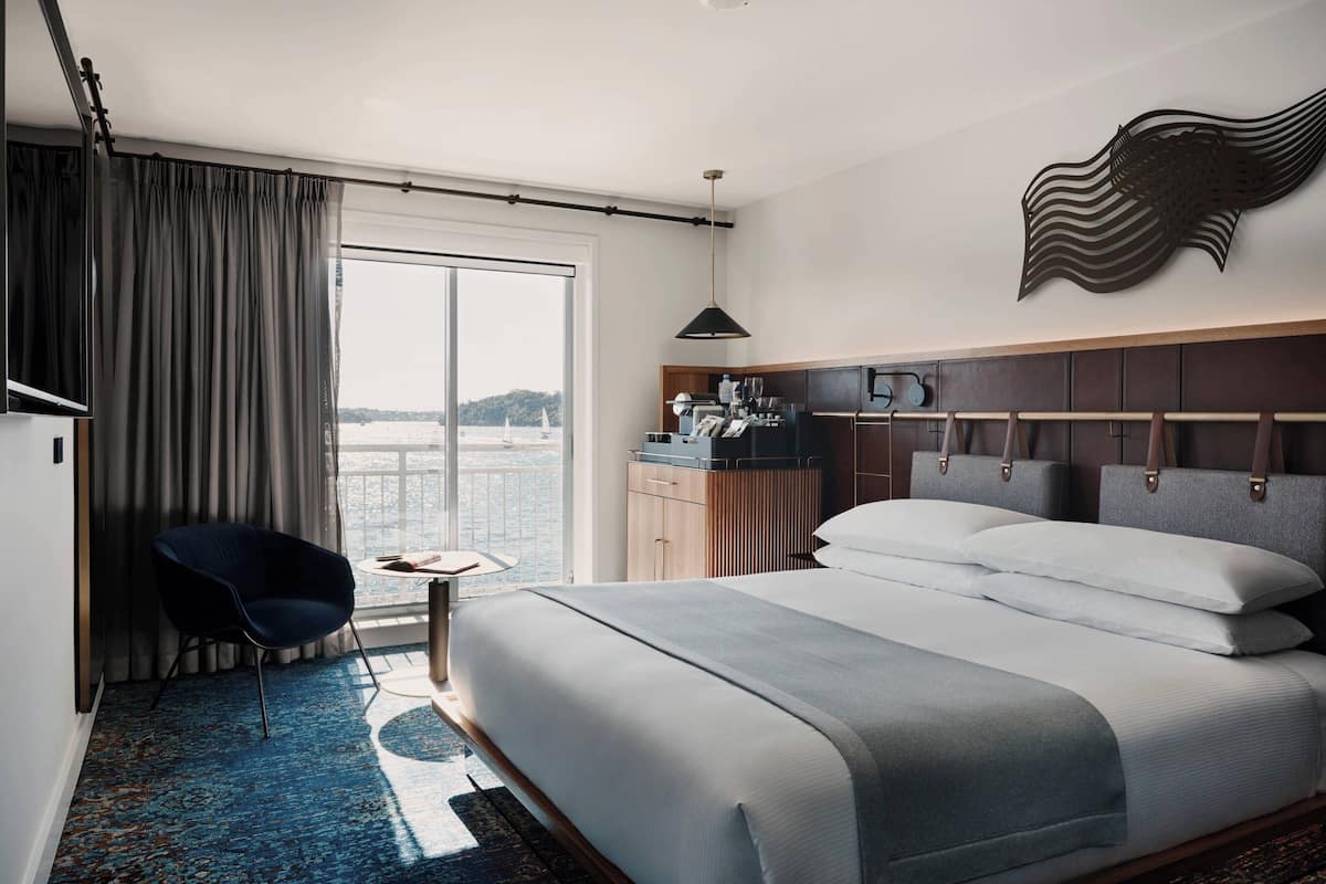 A hotel room with a large bed, a desk with a chair, a view of the sea, and a decorative wall piece.