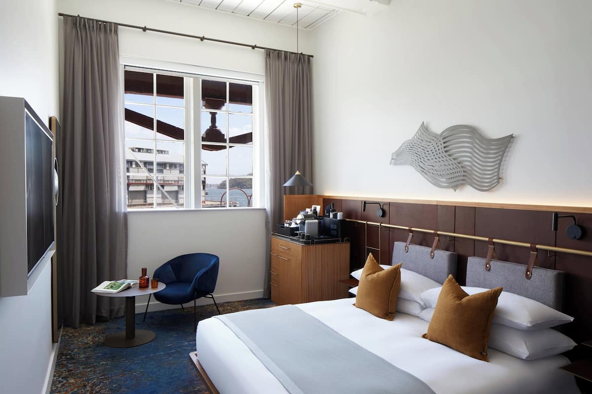 A hotel room with a bed, a desk, a chair, a TV, and a window with curtains.