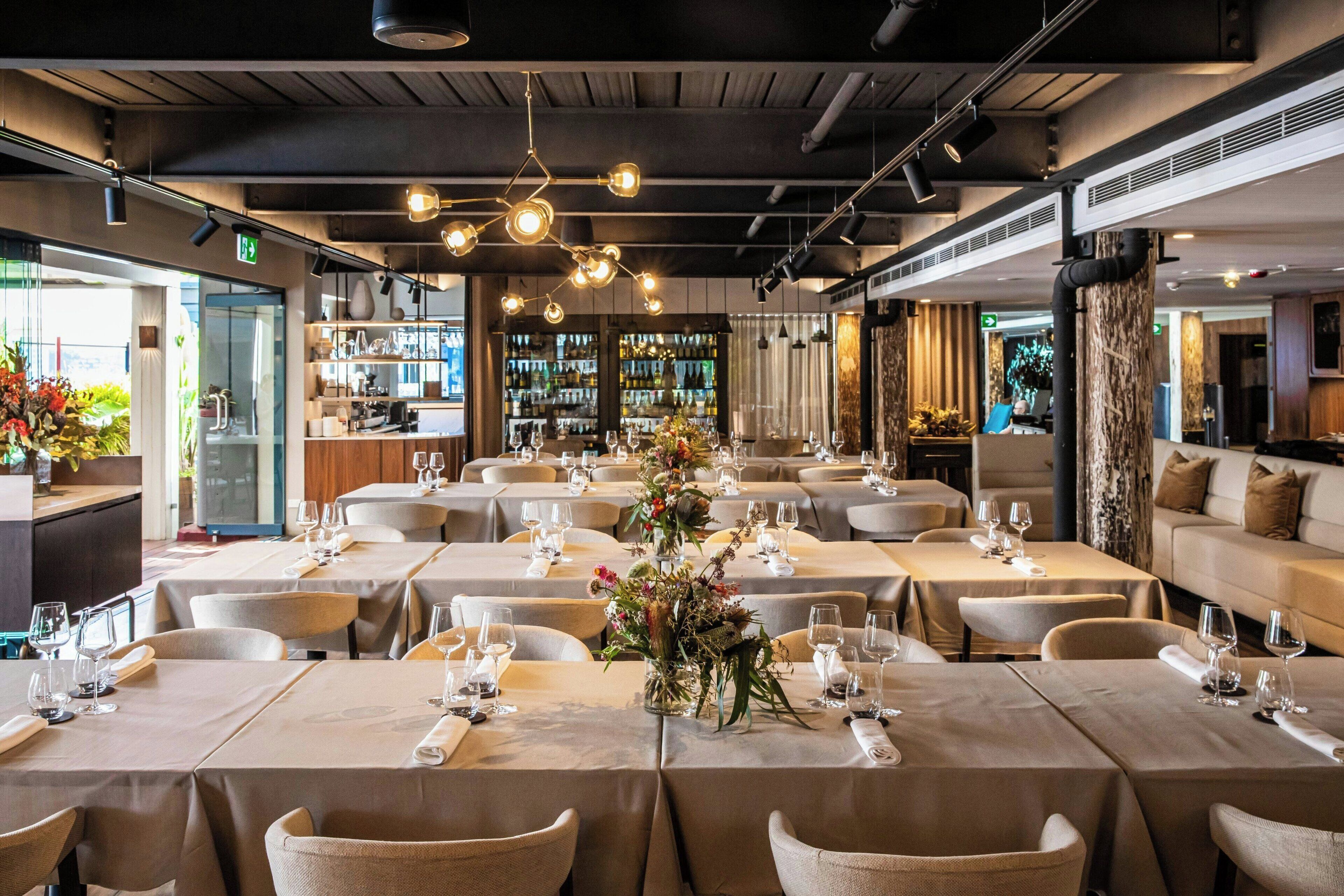A restaurant with multiple tables set for dining, featuring a central floral arrangement.