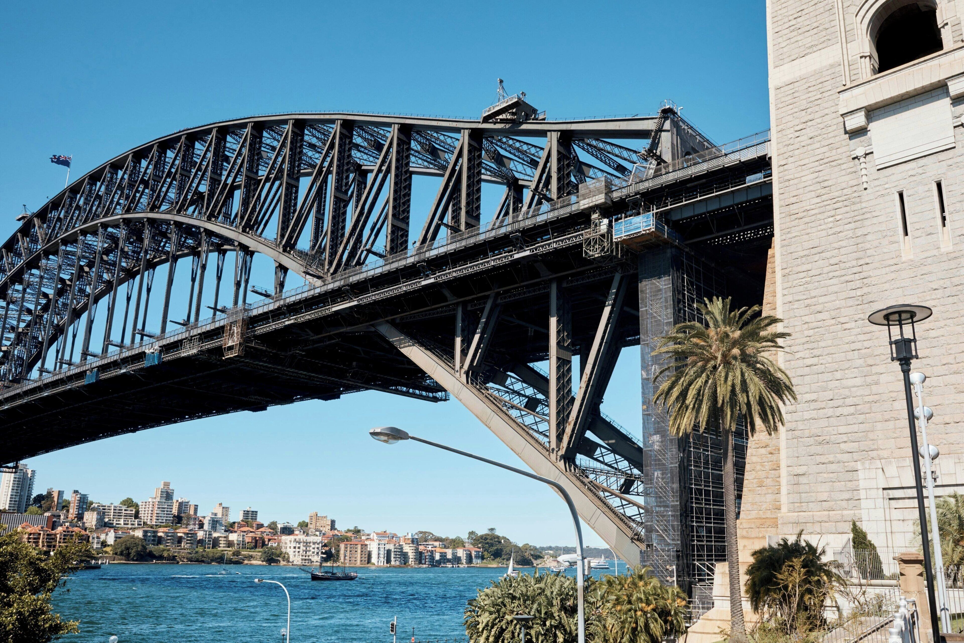 A steel bridge with a curved design spanning over a body of water, with a cityscape in the background.