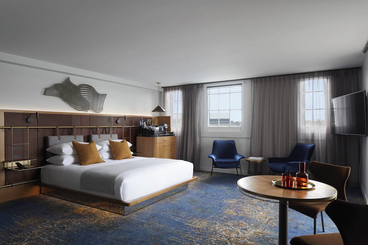 A hotel room with a large bed, a desk with a chair, a round table with a tray, and a TV.