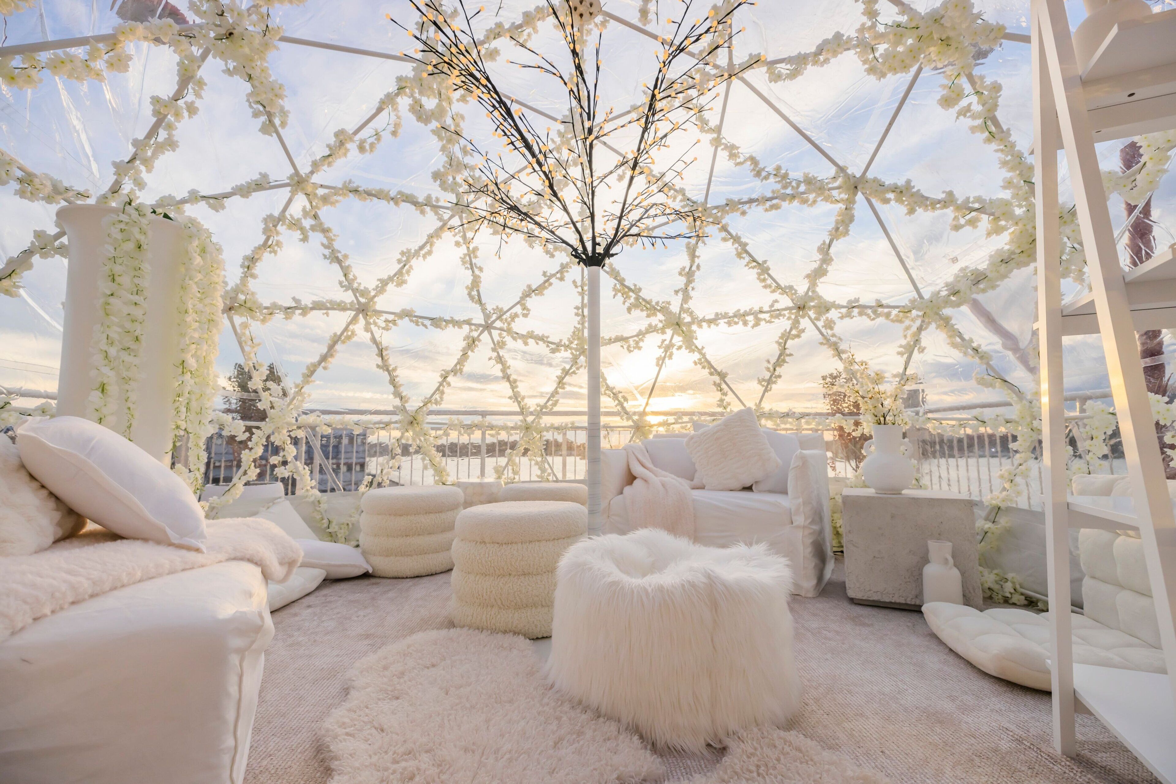 A cozy, white-themed outdoor seating area with plush furniture and a decorative tree.