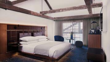 A modern hotel room with a large bed, wooden beams on the ceiling, a desk, and a chair.