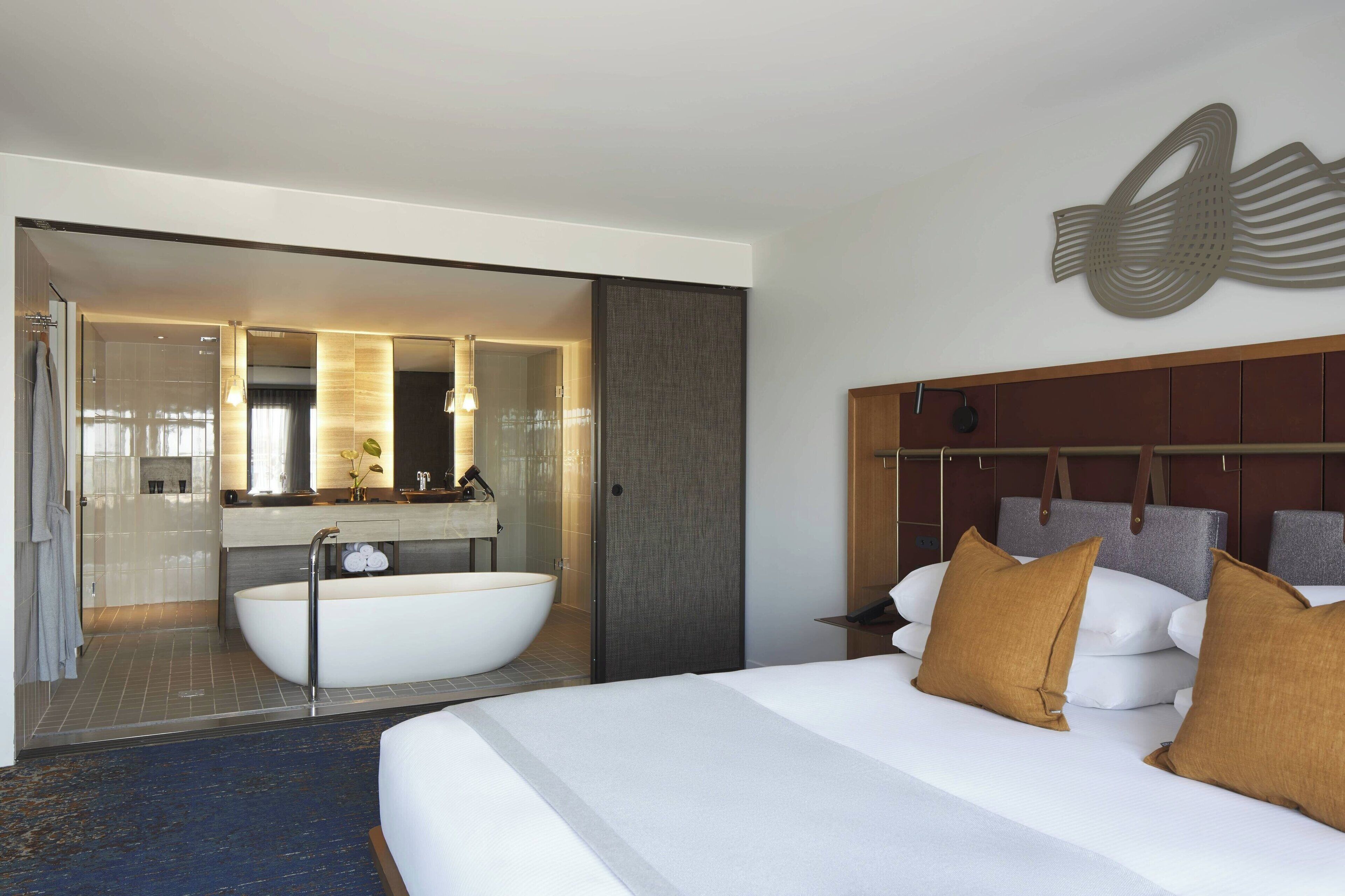 Une chambre d’hôtel moderne dotée d’un grand lit, d’une baignoire et d’une salle de bain séparée avec un miroir.