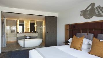 Une chambre d’hôtel moderne dotée d’un grand lit, d’une baignoire et d’une salle de bain séparée avec un miroir.