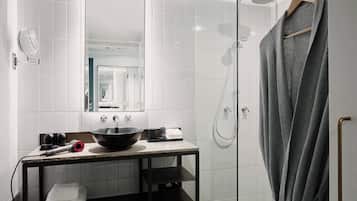 A modern bathroom with a large mirror, a black bowl sink, a towel rack, and a shower area.