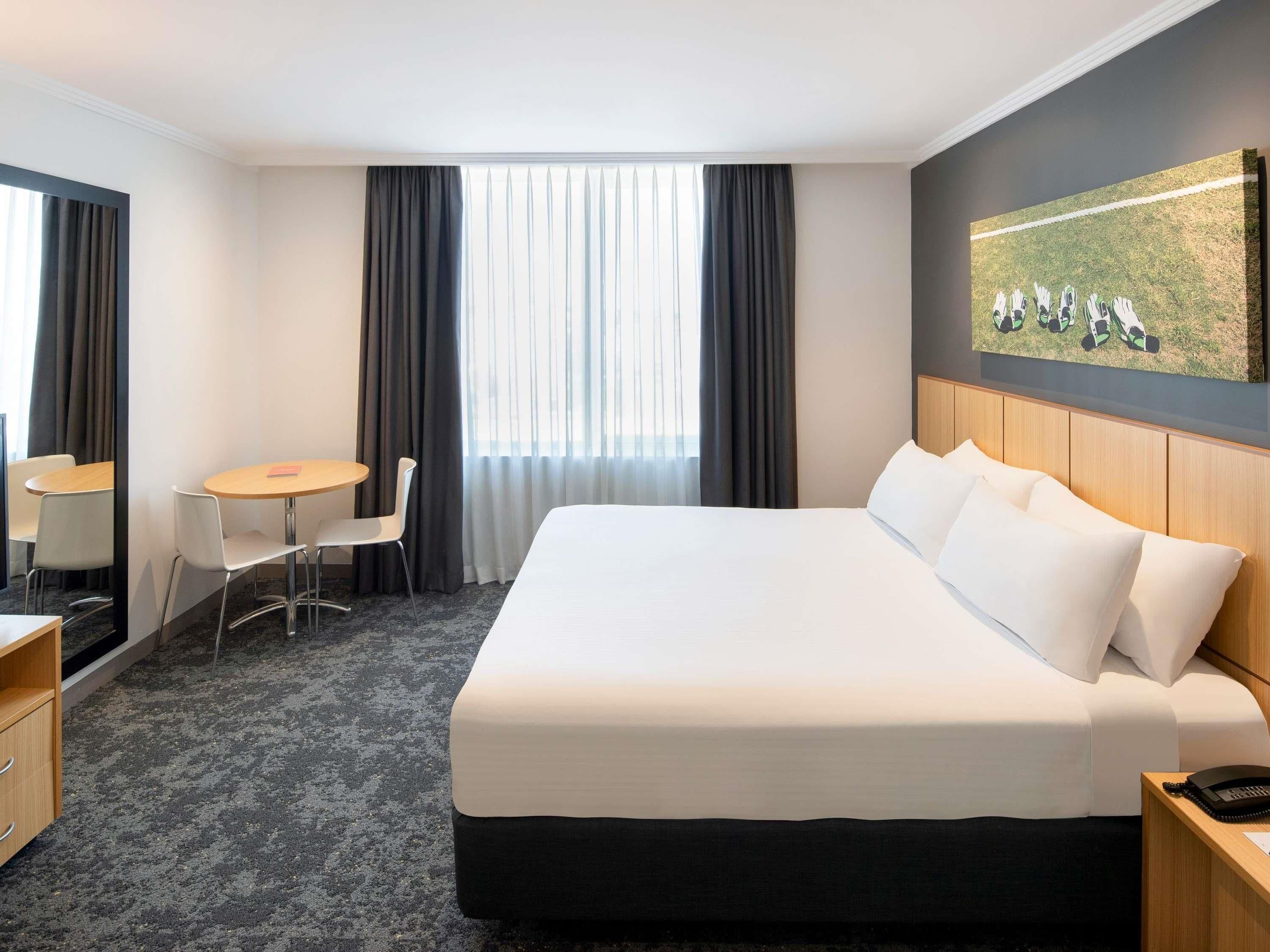 A hotel room with a large bed, a desk, a chair, and a painting on the wall.