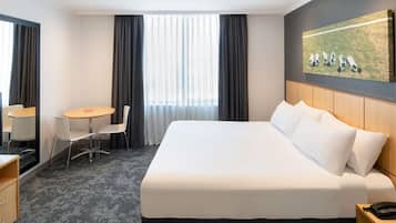 A hotel room with a large bed, a desk, a chair, and a painting on the wall.