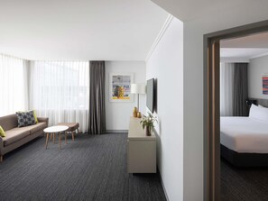 A hotel room with a bed, a sofa, a small table, a TV, and a desk with a lamp and decorative items. - Mercure Sydney Bankstown (Bankstown)