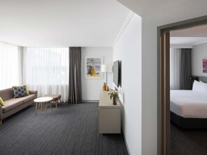 A hotel room with a bed, a sofa, a small table, a TV, and a desk with a lamp and decorative items.