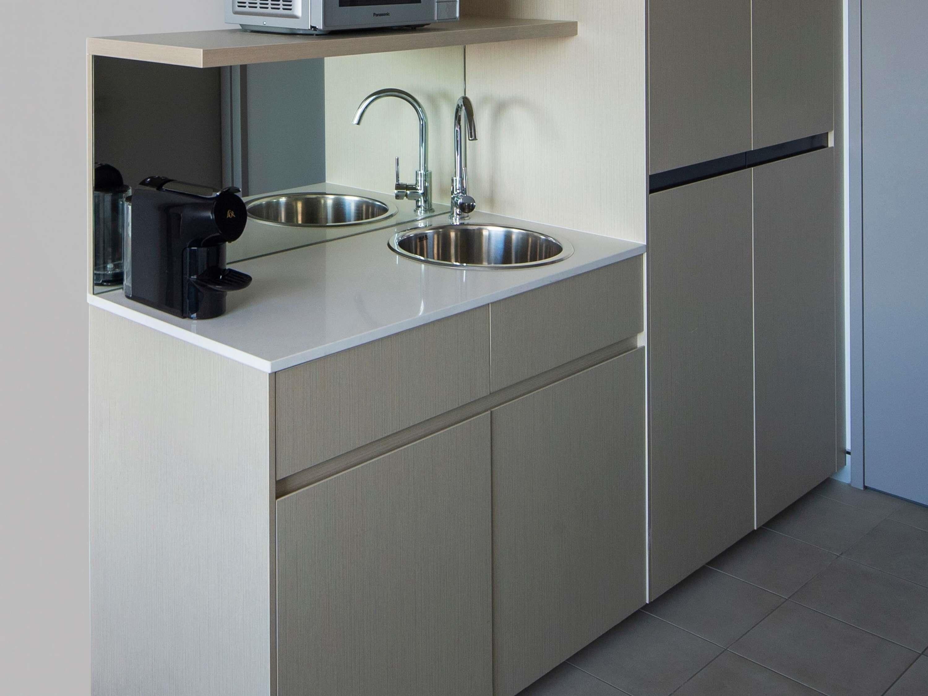 A modern kitchen with a built-in sink, a coffee maker, and a microwave on a light-colored countertop.