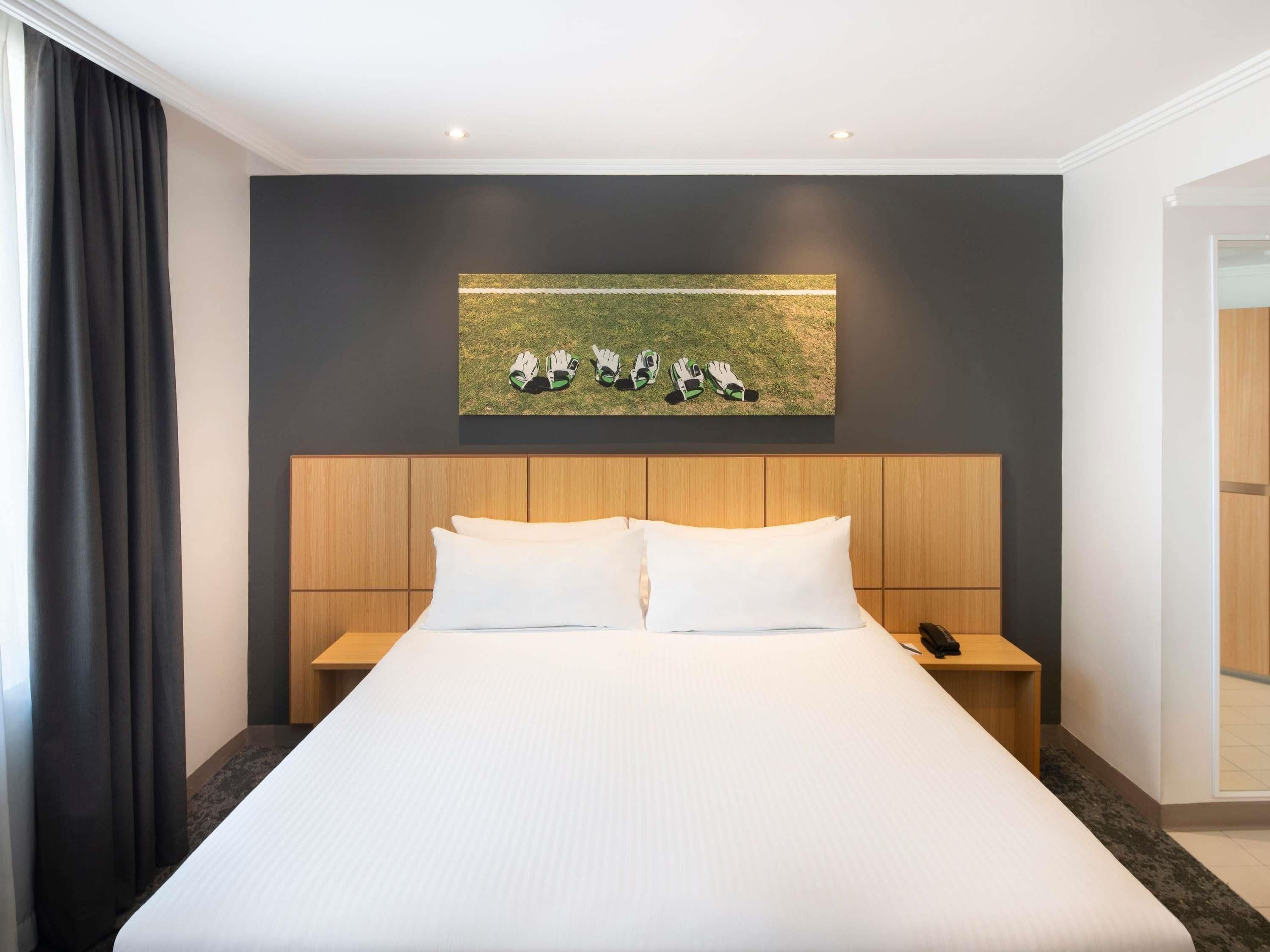 Habitación de hotel con una cama grande, cabecera de madera, dos mesitas de noche y un cuadro con guantes en la pared.