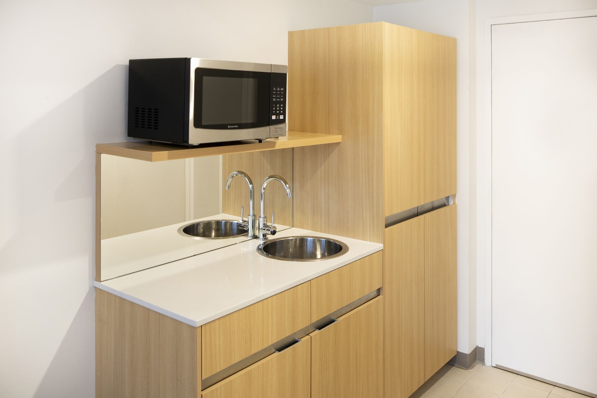 A modern kitchen with a microwave, two sinks, and wooden cabinetry.