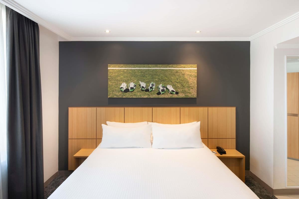 A modern hotel room with a large bed, wooden headboard, and a painting of gloves on the wall.