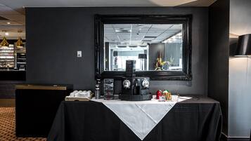 Ein Hotelzimmer mit einem schwarzen Tisch, gedeckt für das Frühstück, einem großen Spiegel und Blick ins Hotelinnere.