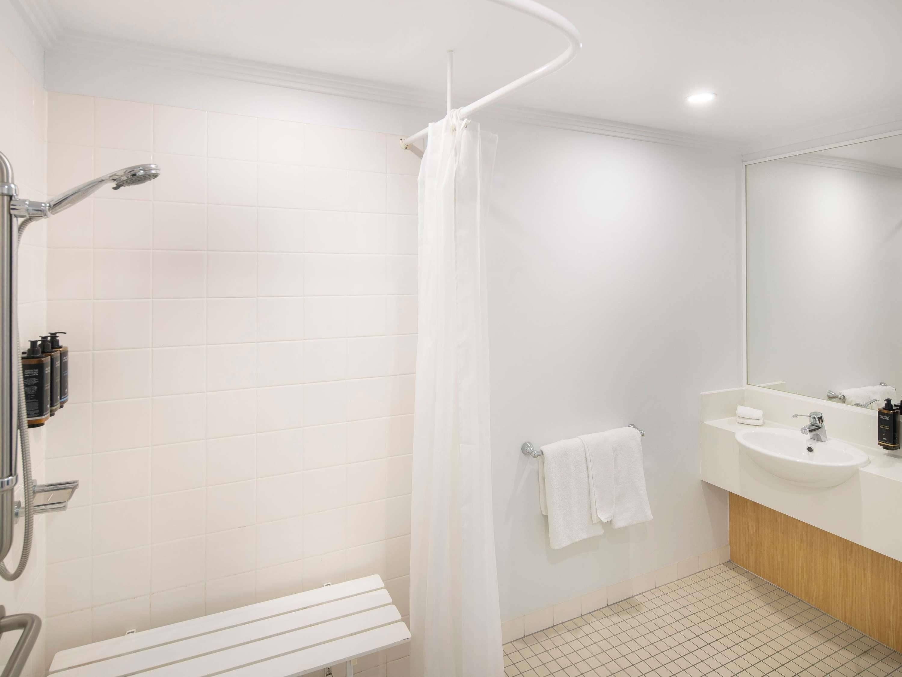 A bathroom with a shower, a bench, a sink, and a mirror.