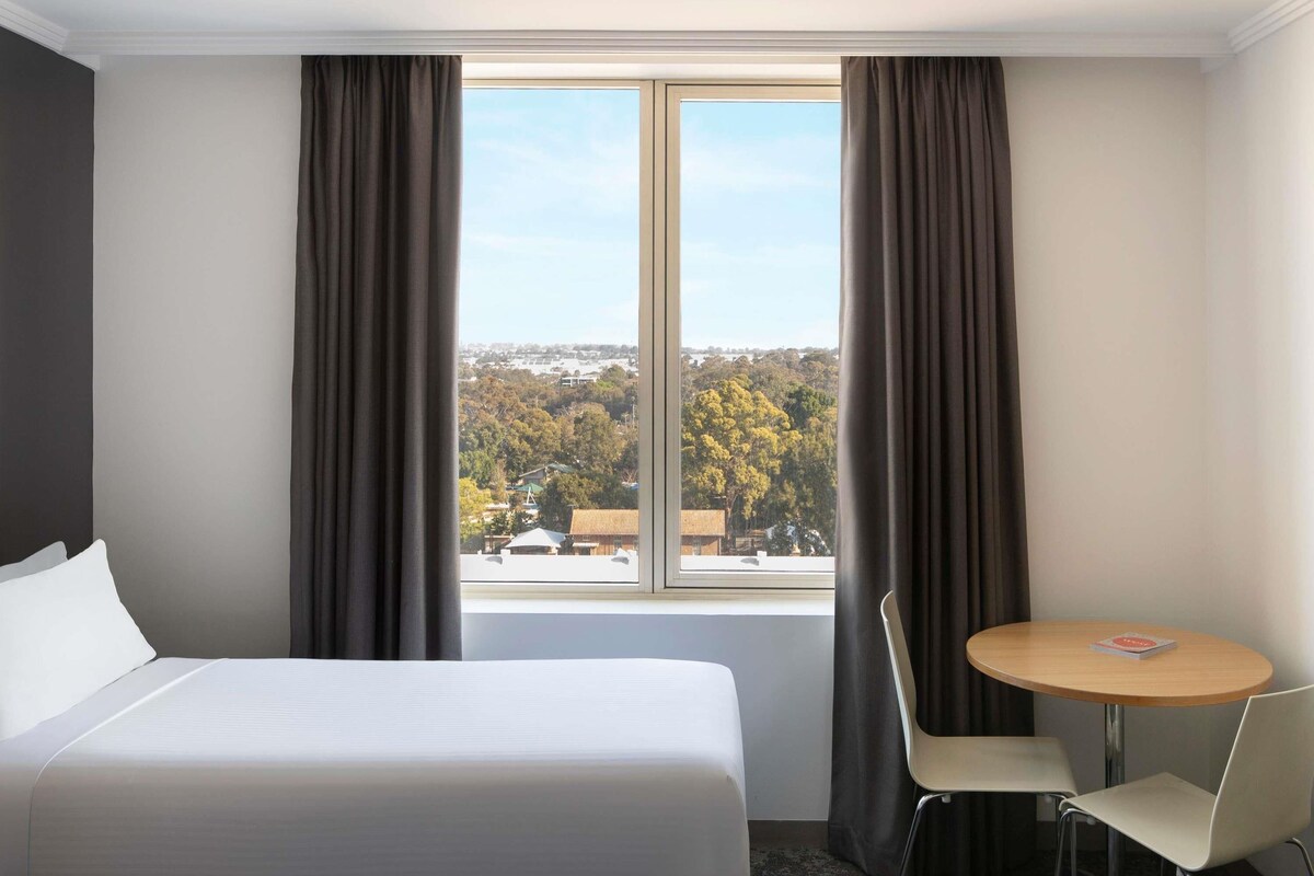 A hotel room with a bed, a round table with two chairs, and a window with curtains.