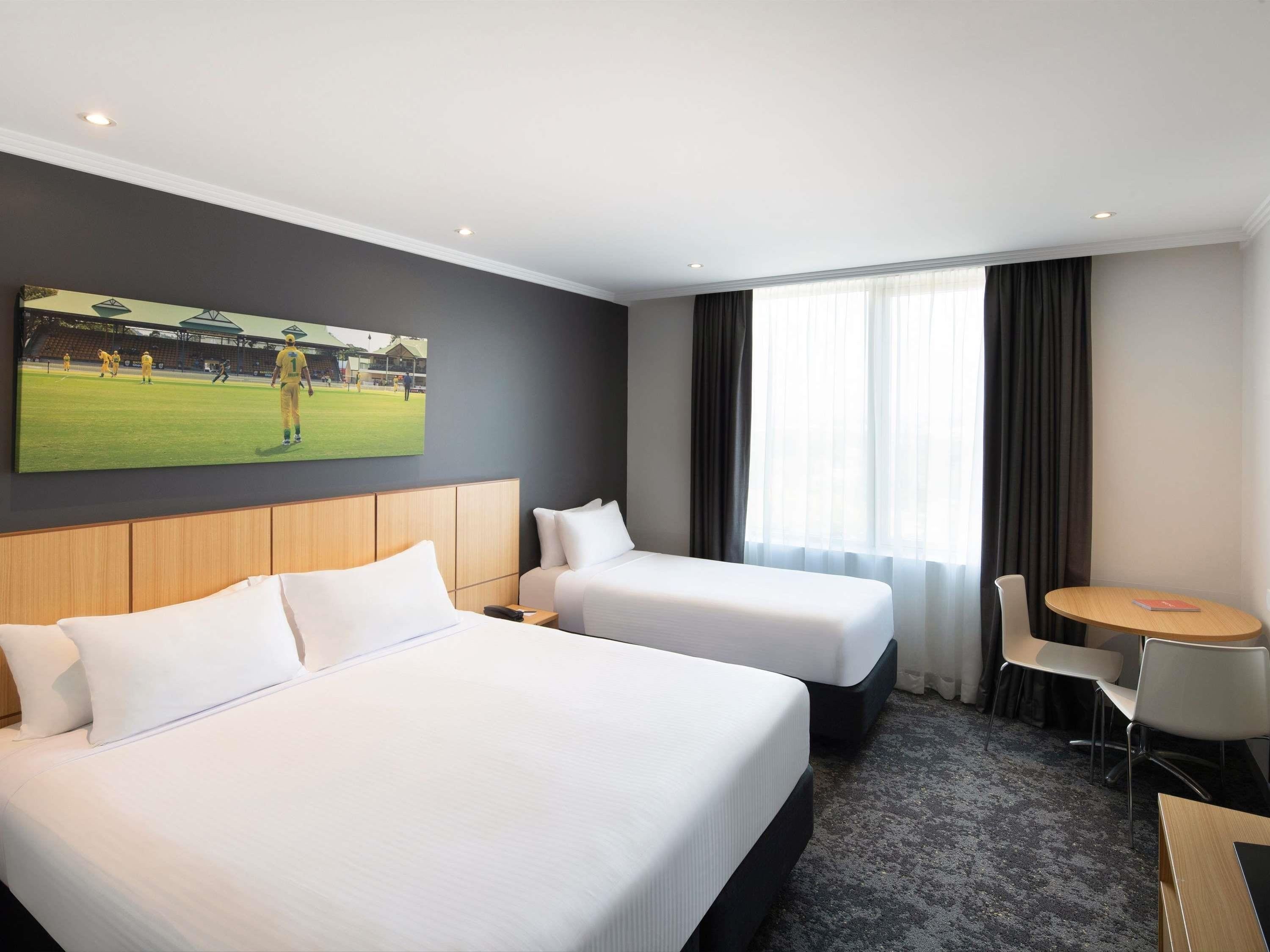 A hotel room with two beds, a small table, and a chair.