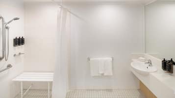 A modern bathroom with a shower, bench, sink, and mirror.