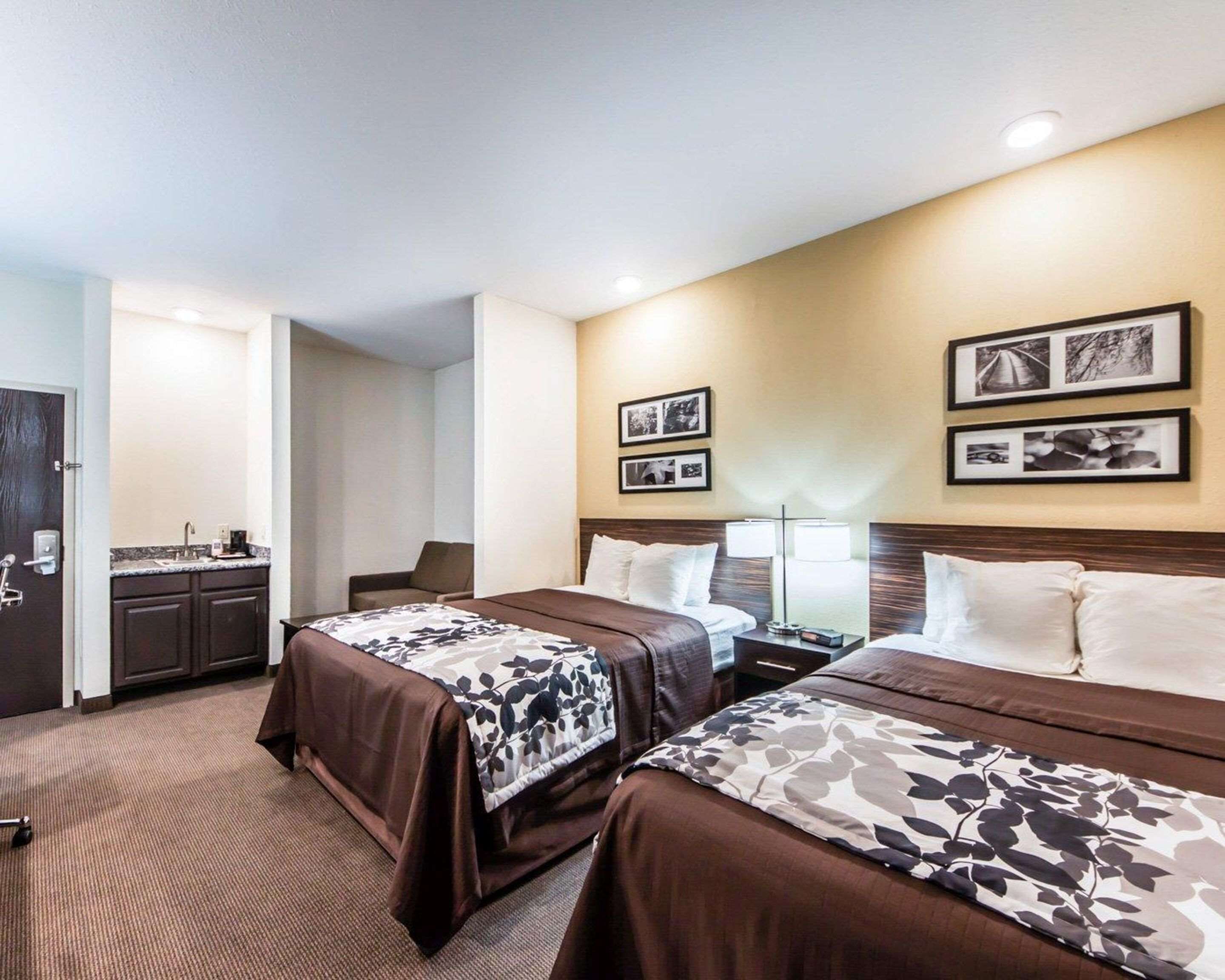 Habitación de hotel con dos camas, un escritorio, una silla, un lavamanos y cuadros en la pared.